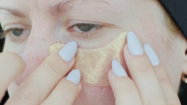 A nő foltokat helyez el egy frissítő maszk szeme alá. Egy nő kollagén párnákkal a szeme alatt. Kozmetikai eljárások. Otthon. Közelkép - Felvétel, videó
