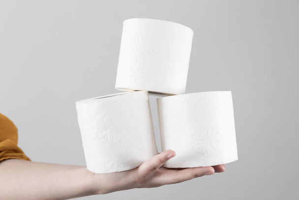 Female hand holds soft toilet rolls on gray background with copy space. Minimal composition for advertisement, article - Fotoğraf, Görsel