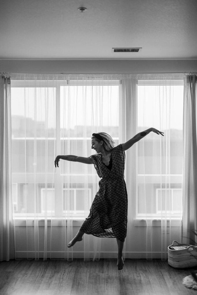 Schwarz-weißes Konzept, Dame tanzt im Maxi-Kleid vor dem Fenster. Ballerina tanzt. Tanzbewegungen. Selbstisolierung bleiben Coronaviren zu Hause. Tänzerin zeigt Nachbarn ihre Tanzbewegungen.Getreidefotos - Foto, Bild