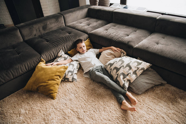 Family in a big house. Lifestyle Home comfort. Children at home. Children playing on the floor. Textile. Teen boy lying on the floor on pillows. Brown sofa, yellow pillows. - Fotografie, Obrázek