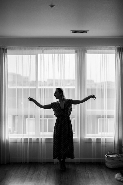 Czarno-białe pojęcie, pani tańczy w maxi sukienka przed oknem. Balerina tańczy. Tańcz. Samodzielne pobyt w domu koronawirus.Dancer pokazuje sąsiadom jej ruchy taneczne.Zdjęcia ziarna - Zdjęcie, obraz