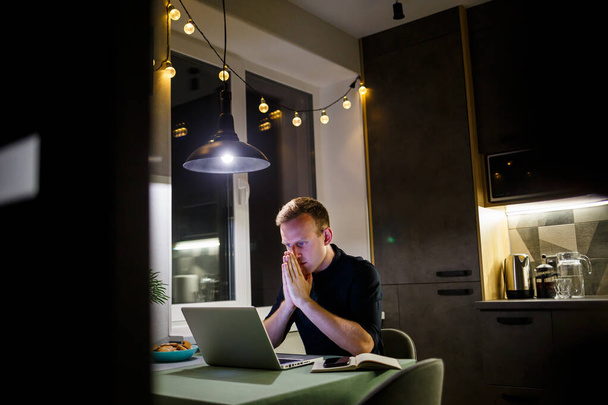 Een freelancer werkt vanuit huis in de keuken en met een laptop. Zakenman werkt met laptop en leest goed nieuws. Succesvolle ondernemer zit en werkt zelfstandig in zijn moderne woning. - Foto, afbeelding