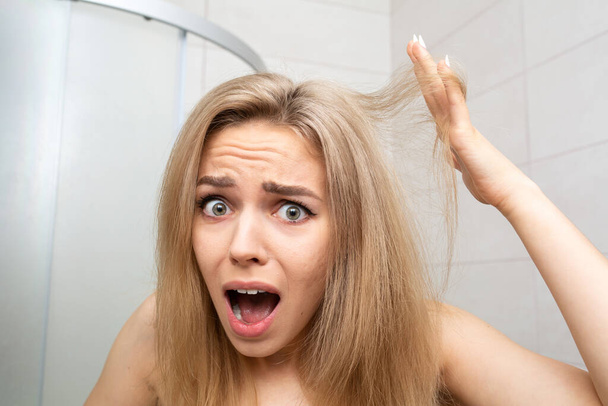 Pretty woman in bathroom looks at tangled hair. - 写真・画像