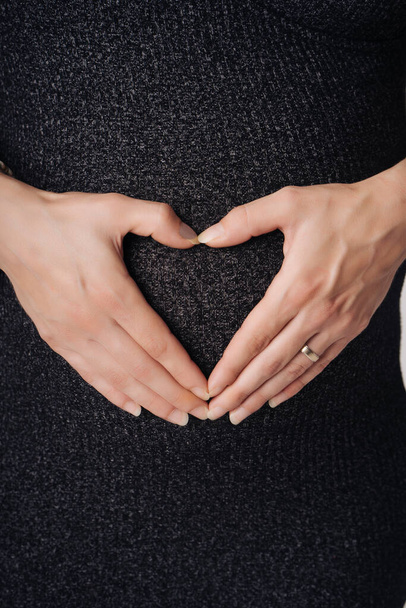 Cropped image of beautiful pregnant woman drawing a heart with her hands on her belly in her room - Foto, Imagen