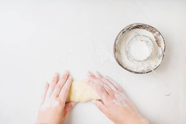 Dough Making Process. Coconut bowl with flour and strainer. Female hand kneading the dough. White background. Top view.  - 写真・画像