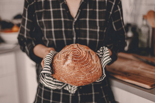 Homemade sourdough bread. Bright white kitchen. Bread on cutting board. Kitchen utensils. Craft authentic bread. Home cooking. Food preparation. Coronavirus covid-19 stay home isolation quarantine. - Fotó, kép