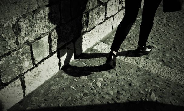 Jambes de femme marchant dans une rue médiévale et son ombre
 - Photo, image