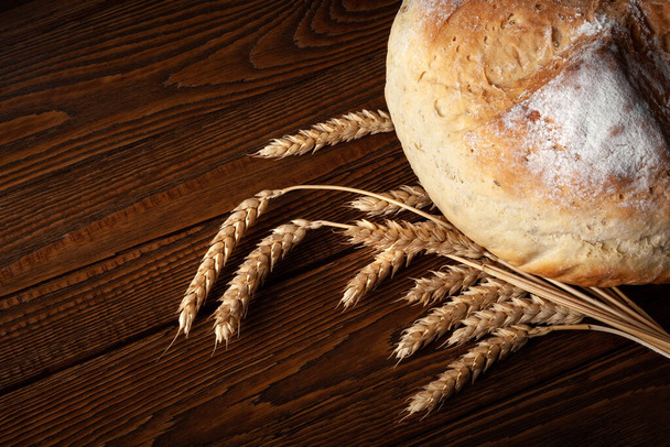Homebaked bread. Loaf of peasant bread and spikelets of wheat on a wooden background. Homemade baking.  - Photo, Image