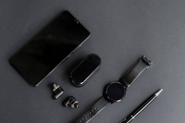 Accessories for men's beauty on a monochromatic background. black pen, black smart watch, smartphone and wireless headphones on dark background. View from above. Minimalist black trend 2020. - Fotó, kép