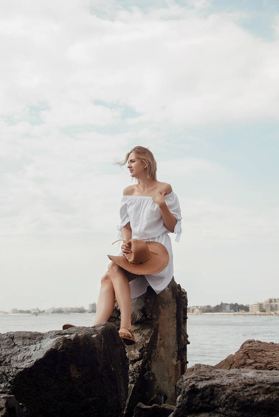 Νεαρή γυναίκα δίπλα στη θάλασσα. Όμορφο κορίτσι με λευκό φόρεμα και καπέλο στις διακοπές. Ταξίδι στη Μαύρη Θάλασσα. - Φωτογραφία, εικόνα