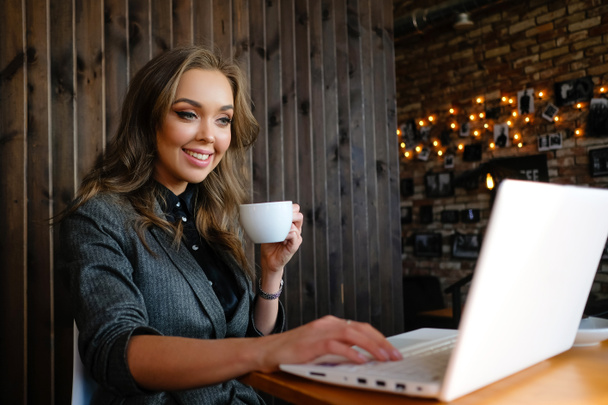 Όμορφη επιχειρηματίας πίνει καφέ και δουλεύει σε ένα καφέ. Κορίτσι που αγοράζει στο Διαδίκτυο και επικοινωνεί στα κοινωνικά δίκτυα. - Φωτογραφία, εικόνα