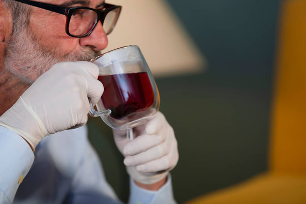 άνθρωπος με ιατρικά γάντια πίνοντας ένα φλιτζάνι τσάι - Φωτογραφία, εικόνα