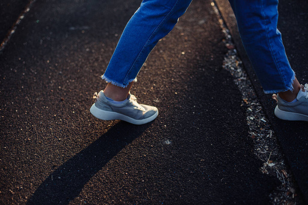 Décidez par où aller. Promenade route caoutchoutée. Jambes féminines en jean et baskets grises. l'ombre des pieds sur le sol
. - Photo, image