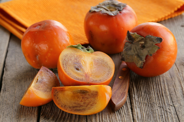 Persimmon fruit whole and sliced on a wooden table - Fotografie, Obrázek