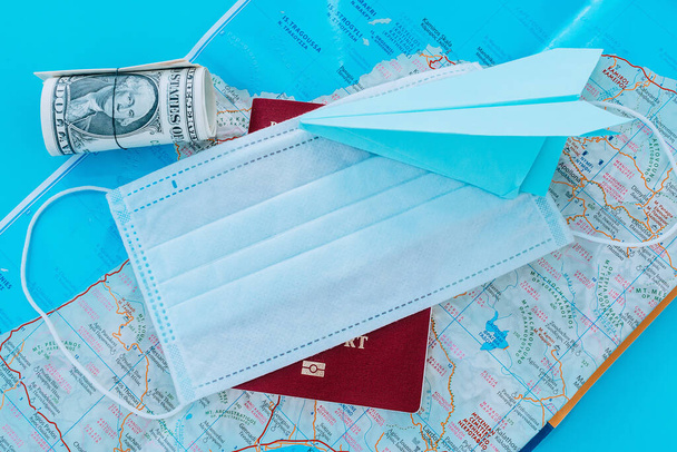 Blue paper airplane,protective mask,dollars and passport on the background of a Greece's map.Concept of a flight ban due to coronavirus pandemic. - Photo, Image