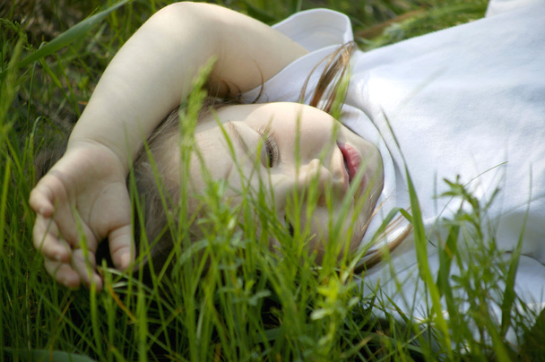 Гарна маленька дівчинка лежить на зеленій траві
 - Фото, зображення