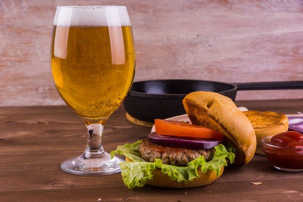 Składniki domowej roboty hamburgera i szklanka piwa na drewnianym stole - Zdjęcie, obraz