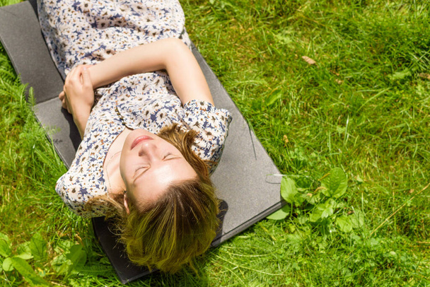 Joven mujer atractiva se encuentra en una alfombra en el césped en verano en un día soleado
 - Foto, imagen