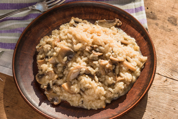 Włoskie tradycyjne danie - risotto z grzybami w glinianej płycie na starym drewnianym stole, widok z góry, miejsce na kopię przepisu - Zdjęcie, obraz