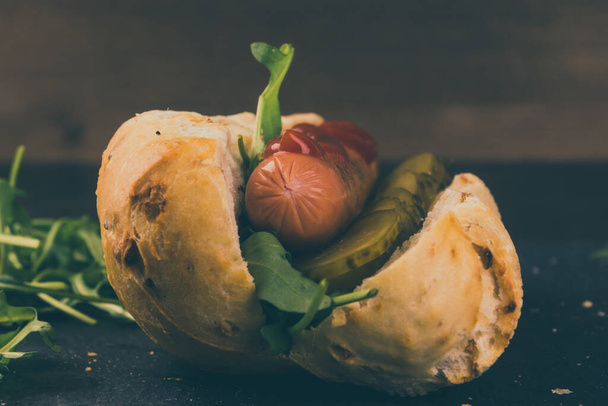 ホットドッグ、パンとソーセージ、サラダと暗めの背景にキュウリの漬物 - 写真・画像