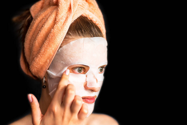 Mujer joven se endereza con máscara de lámina cosmética sobre fondo oscuro - espacio para copiar, concepto de cuidado facial
 - Foto, imagen
