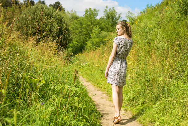 Bela jovem caminhando através de um prado contra um céu azul com nuvens
 - Foto, Imagem