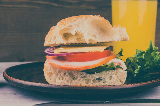 Сэндвич с ветчиной, сыром, салатом, луком и помидорами на темном деревянном фоне крупным планом
 - Фото, изображение