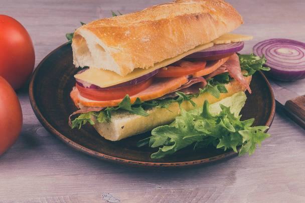 Свіжий бутерброд з багета з шинкою, сиром, салатом, цибулею та помідорами
 - Фото, зображення