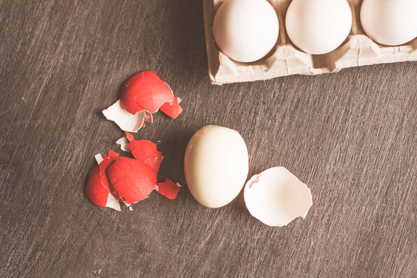 Яйцо красное сломанная скорлупа и картонная коробка с белыми яйцами
 - Фото, изображение