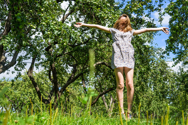 Jonge aantrekkelijke vrouw in korte jurk springen in de tuin - Foto, afbeelding
