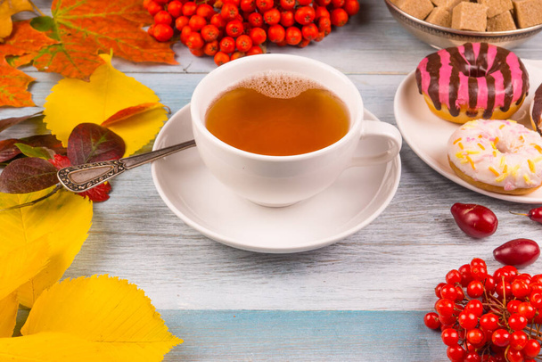 cup of tea and donuts with colorful autumn leaves and berries on a rustic wooden background - Fotografie, Obrázek