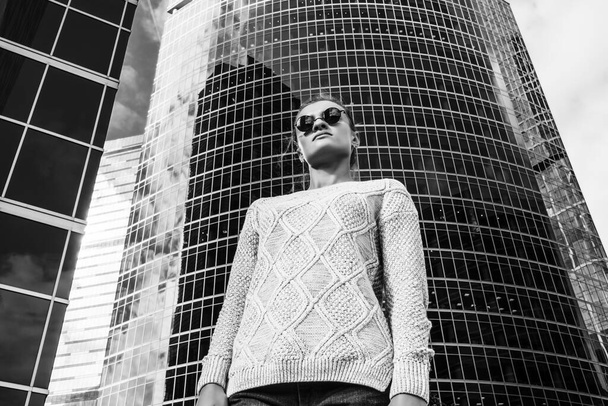 jovem mulher em óculos de sol em um fundo de alto centro de negócios
 - Foto, Imagem