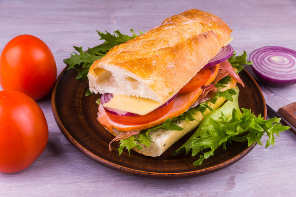 Friss bagett szendvics sonkával, sajttal, salátával, hagymával és paradicsommal - Fotó, kép
