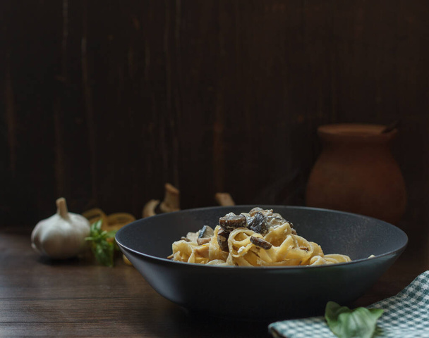 Hot homemade pasta with wild mushrooms in a gray plate close-up on a dark wooden background, horizontally with space - Foto, imagen