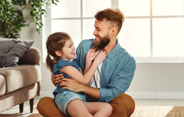 Fröhlicher junger Mann umarmt kleine Tochter, während er zusammen auf dem Boden sitzt und in der Freizeit im modernen, hellen Wohnzimmer spielt - Foto, Bild