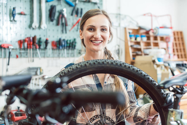 Bike mechanic woman looking through the wheel of bicycle - Foto, afbeelding