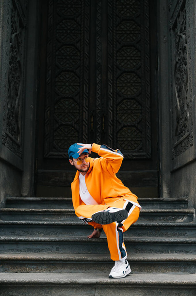 Bright hip hop dancer performing on a dark door of an old building. Street dancing. Hip hop dancer dancing Break Dance on the street on a background of historic architecture and looking away. Vertical - Фото, изображение