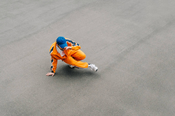 Pouliční tanečnice v oranžových šatech tančící hip hop na šedém asfaltovém pozadí, horní pohled. Muž ve stylových neformálních šatech tančí taneční tanec na asfaltovém chodníku. Pozadí.Kopírovat mezeru - Fotografie, Obrázek