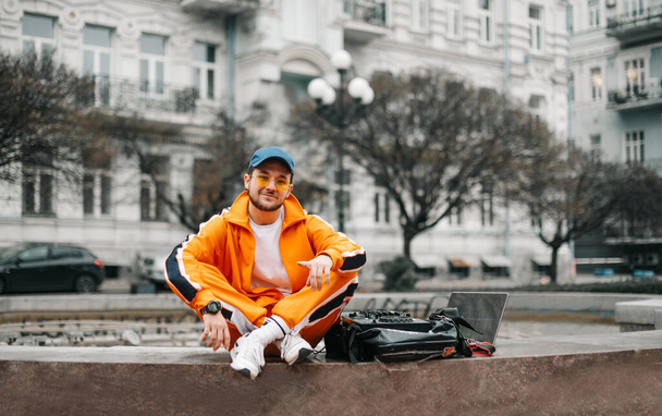 Hymyilevä DJ istuu äänen mikseri ohjain ja kannettava tietokone kadulla, soittaa musiikkia asettaa, tutkii kameraan ja hymyilee Street kuva hip hop DJ ulkona
. - Valokuva, kuva