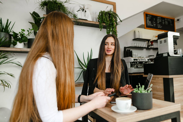 İki genç iş kadını rahat bir kafede oturmuş projeleri tartışıyor ve kahve içiyorlar. İki kız arkadaş resmi kıyafetler içinde bir kafede kahve içerken sohbet ediyorlar. İş toplantısı - Fotoğraf, Görsel