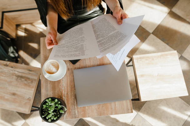Düz bir fotoğraf, kafeteryada oturan iş kadını bir fincan kahve ve iş gazetesi okuyor. Ofis çalışanı kahve molasında belgeleri okur. Boşluğu kopyala - Fotoğraf, Görsel