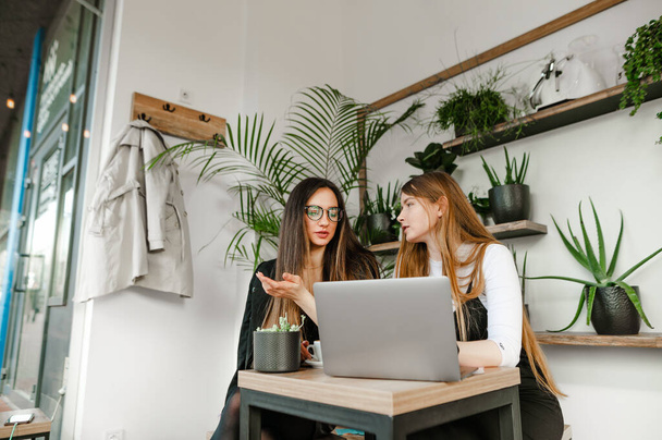 Дві бізнес-леді колеги, сидячи в яскравому стильному ноутбуці, обговорюють роботу з серйозними обличчями. Зустріч двох офісних працівників дівчат у кав'ярні на перерву. Ділова зустріч у кав'ярні
 - Фото, зображення