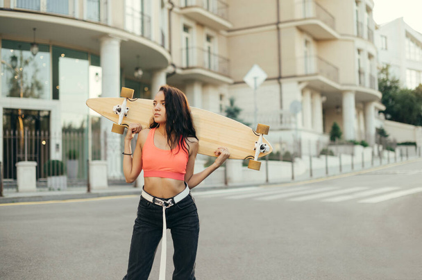 Stílusos lány gördeszka áll az utcán egy longboard a kezében, nézett félre egy komoly arc. Egy spanyol lány arcképe gördeszkával a sétányon. Fénymásolási hely - Fotó, kép