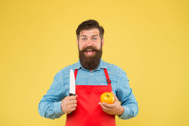 bearded man in red apron with yellow tomato. cooking healthy and fresh food. Handsome male chef is working. mature cook cut vegetable. guy in uniform on kitchen. vitamin dieting - Foto, immagini