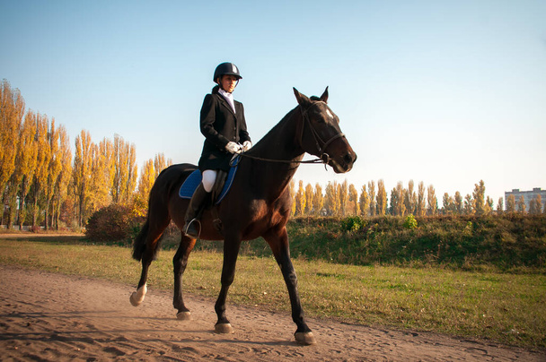 美しい笑顔の女の子ジョッキースタンド彼女の茶色の馬の横に特別な着て - 写真・画像