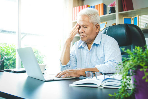 Az idős ázsiai férfi az irodában ült. Stresszes és beteg. Nyugdíjazási koncepció, nyugdíjas egészségbiztosítás - Fotó, kép