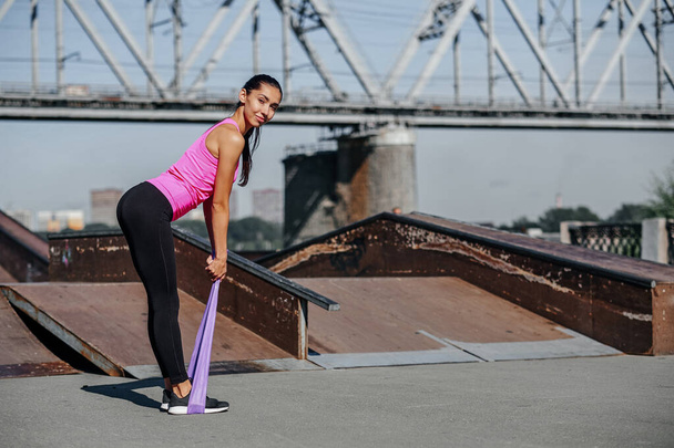 Fitness woman doing stretching exercises with elastic rubber band on urban city background. - Φωτογραφία, εικόνα