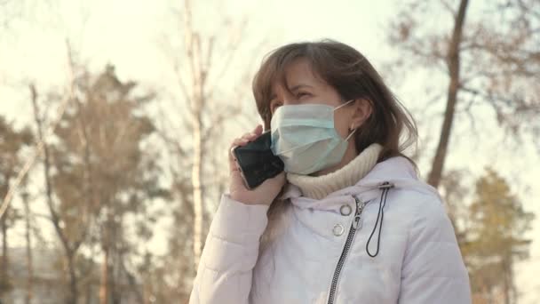 医療保護マスクの若い女性がヨーロッパの街の通りにスマートフォンを持って座っています。コロナウイルス対策。ストリートの観光客はウイルスから保護マスクを着用する。健康と安全を - 映像、動画