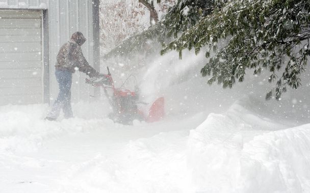 Человек очищает снег во время зимней бури снегоочистителем
 - Фото, изображение