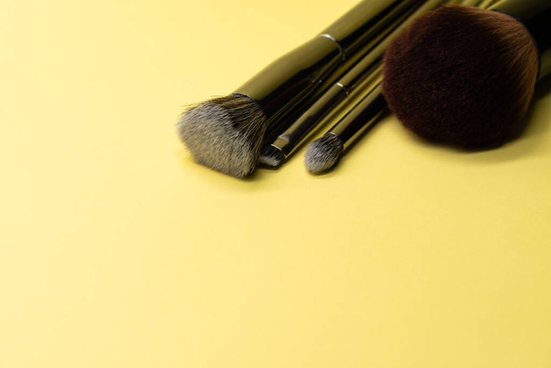 Sarı arka planda gümüş saplı profesyonel makyaj fırçaları ve fotokopi alanı. Güzellik ve yüz estetiği kavramı - Fotoğraf, Görsel